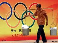 Man carrying two buckets walks by a poster with the Olympic rings