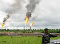 A Nigerian policeman standing in front of burning gas flares  