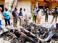 Onlookers and security staff gather around a car destroyed in a blast next to St. Theresa Catholic Church in Madalla, Nigeria, Sunday,