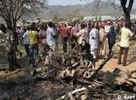 Onlookers  gather around a car destroyed in a blast next to St. Theresa Catholic Church in Madalla, Nigeria,