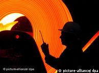 The shadow of a man wearing a helmet against the glowing background of a steel plant