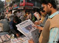 Man on a busy street holding a newspaper with headlines about the attack