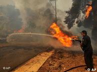 Firefighter shoots water onto a burning tree near a road as smoke rises in the background