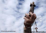 A woman's hand holding a crucifix and statue of a Catholic priest