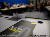 Schwarzes Buch mit grauer Zehn auf dem Titel liegt am dem Pressekonferenztisch (Foto: dpa)