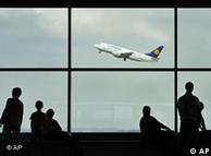 Passengers wait in a terminal as a plane takes off behind them