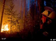 A firefighter looks at a blaze ahead of him in trees