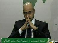 Seif al-Islam, son of Moammar Gadhafi, sits with hands pressed together giving an address on Libyan state television